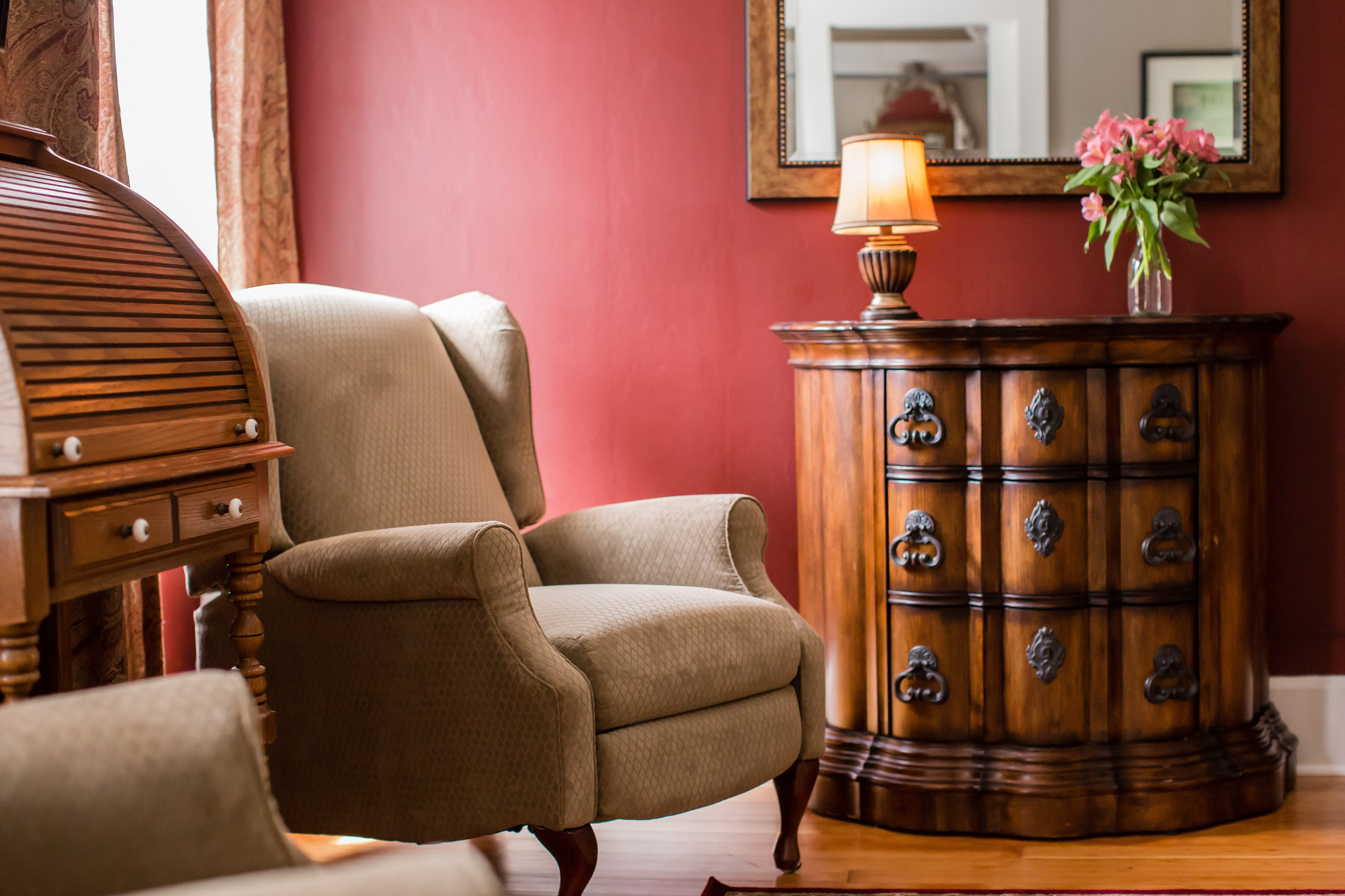 Bordeaux room tan arm chair, wooden roll top desk and dresser with red walls