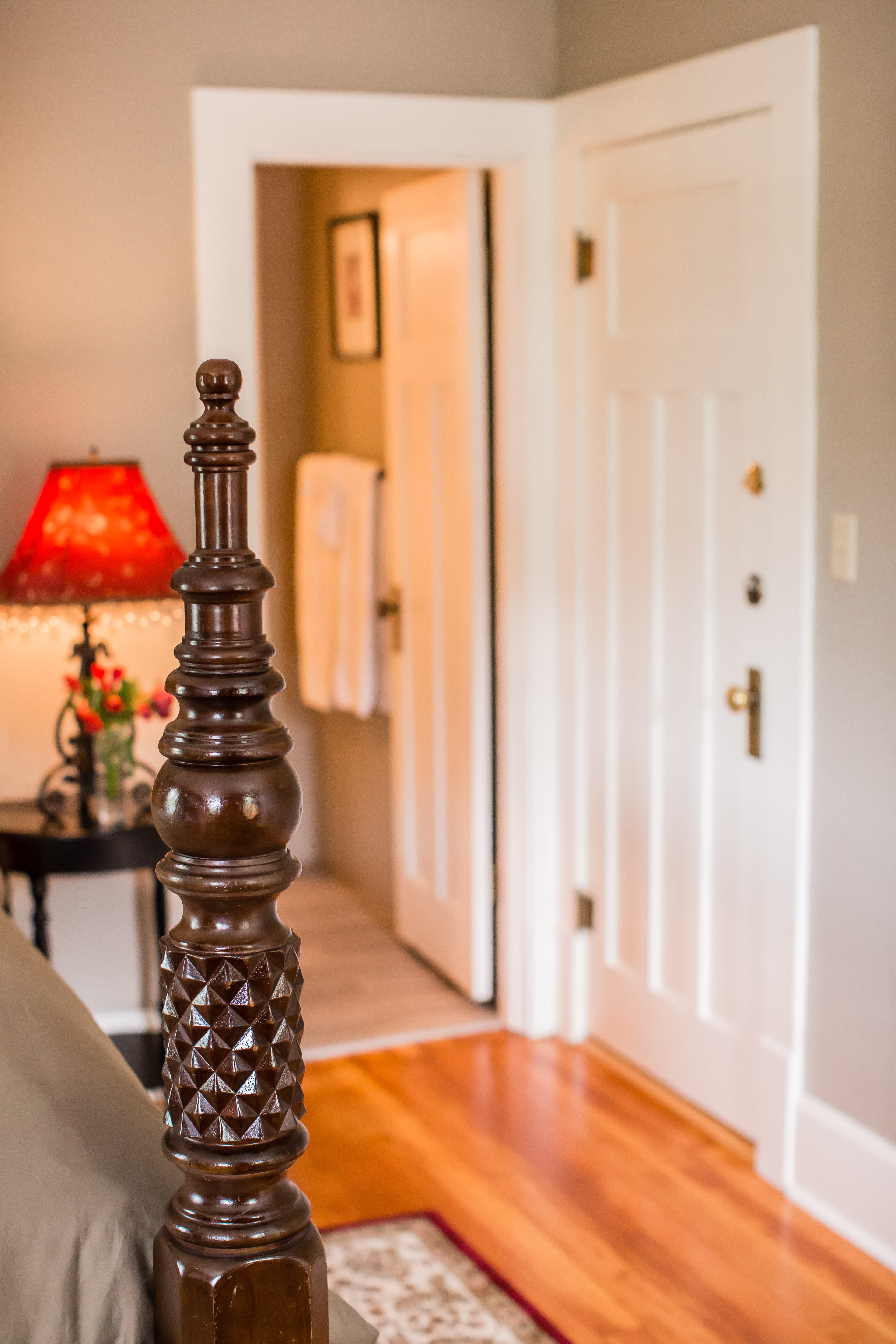 Bordeaux room view toward bathroom with tan walls, red lamp and wood floors