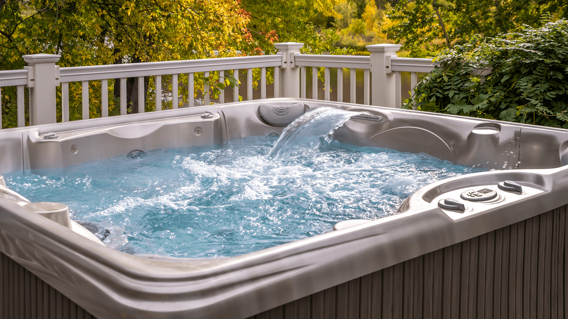 A hot tub filled with bubbling water is surrounded by a wooden railing and autumn foliage.