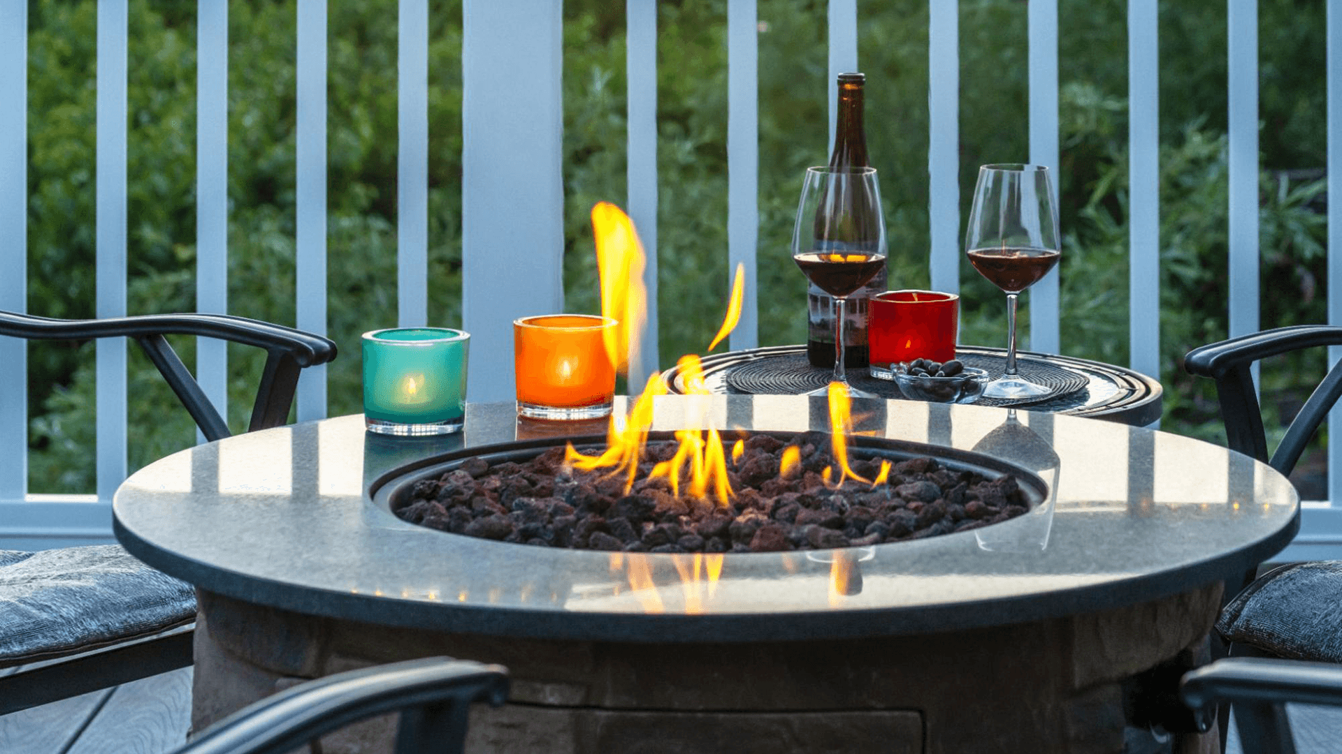 A cozy outdoor setting featuring a fire pit surrounded by colorful candles and glasses of wine.