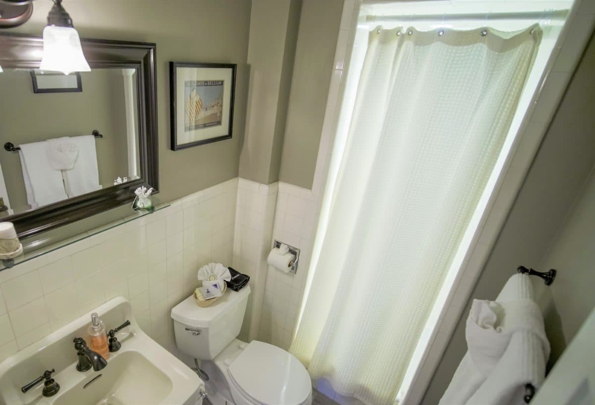 A clean, well-lit bathroom featuring a toilet, sink, and shower curtain with a framed picture on the wall.