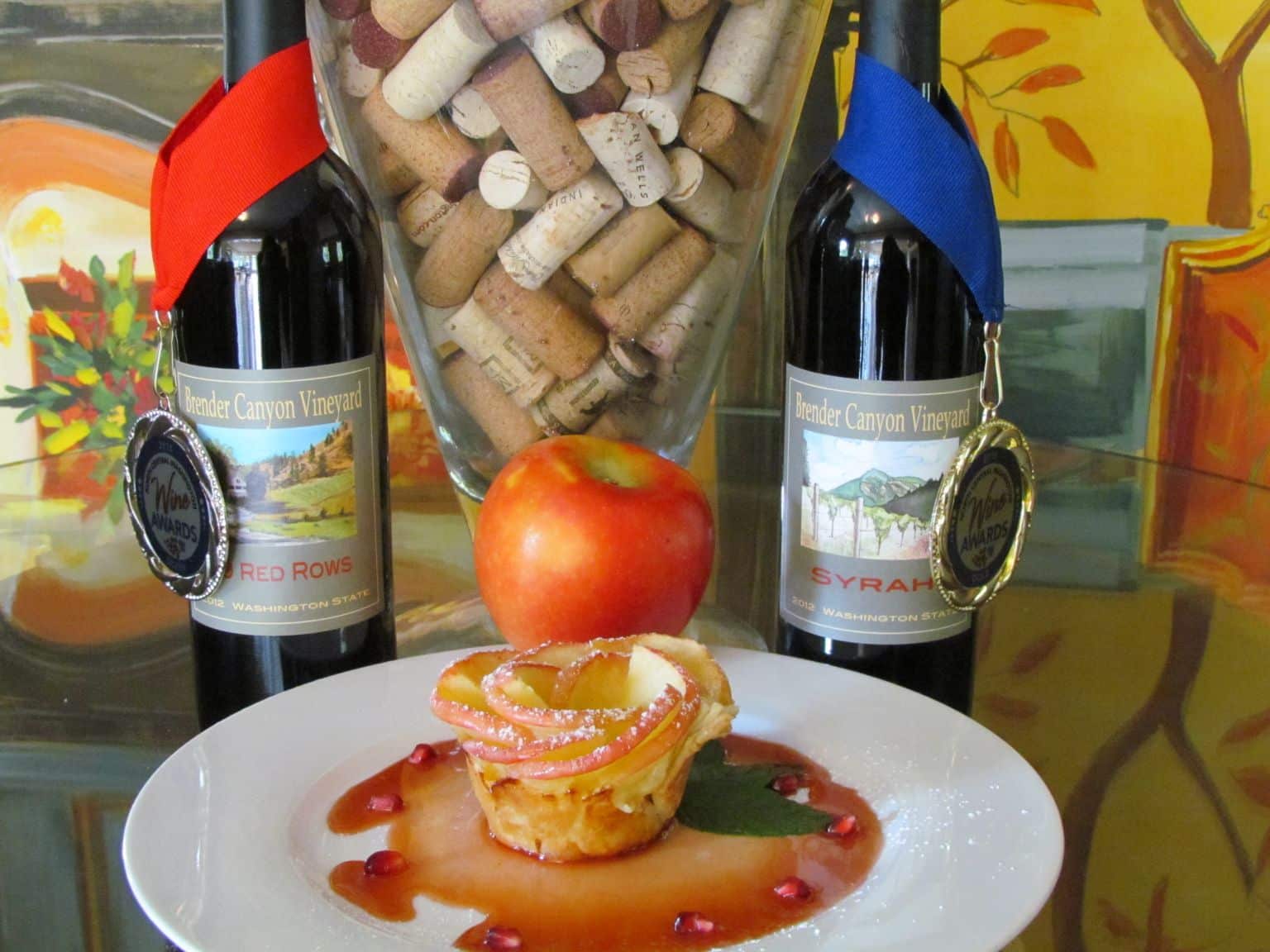 A plate of dessert garnished with apple slices and pomegranate seeds, accompanied by two award-winning bottles of Brender Canyon Vineyard wine.